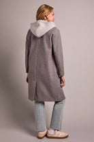 Person wearing a gray coat with a hood on a plain background