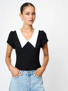 Woman wearing a black top with a white collar and blue jeans on a plain background