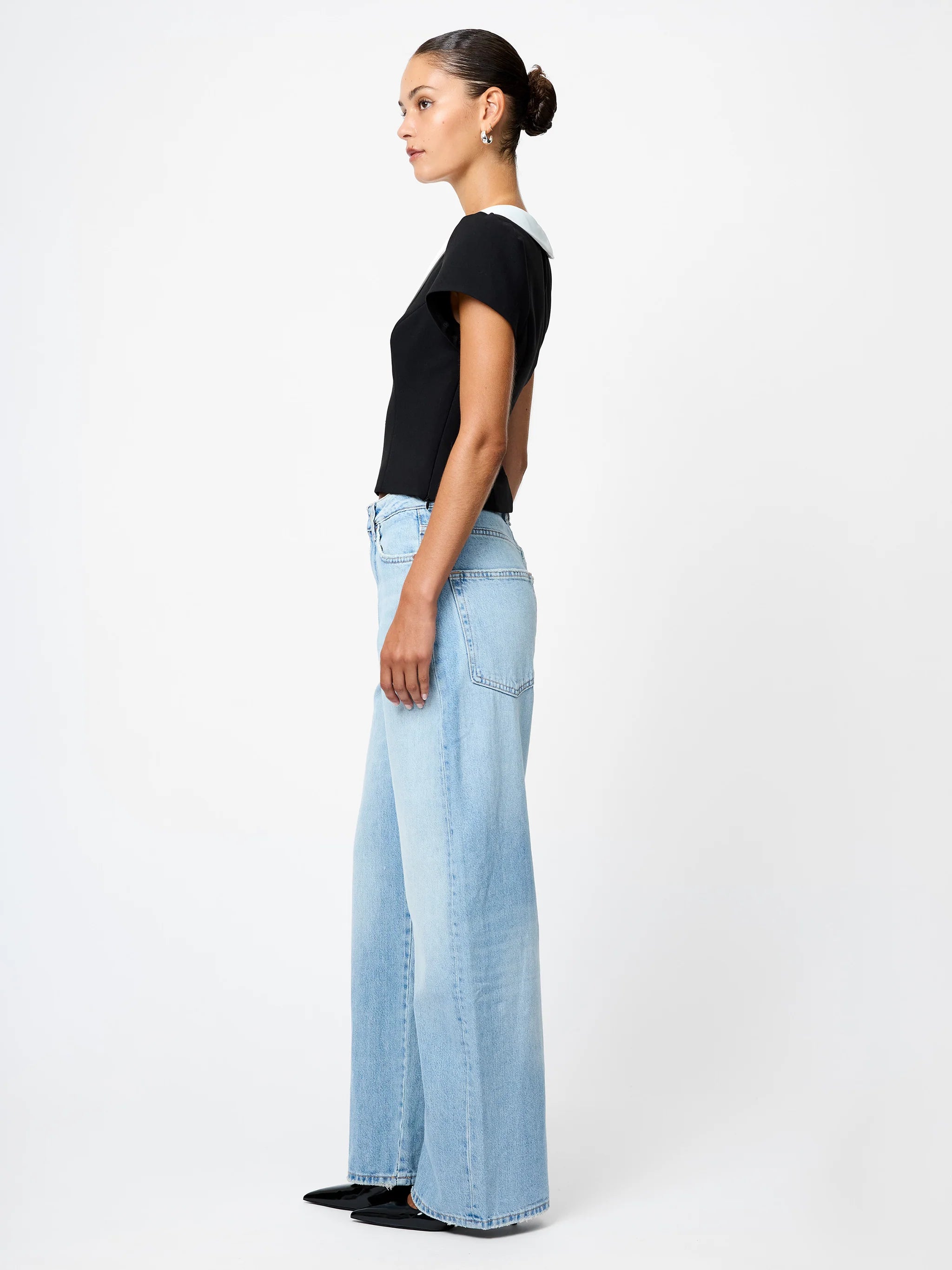 Woman wearing light blue jeans and a black top on a white background