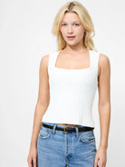 Woman wearing a white sleeveless top and blue jeans on a light gray background