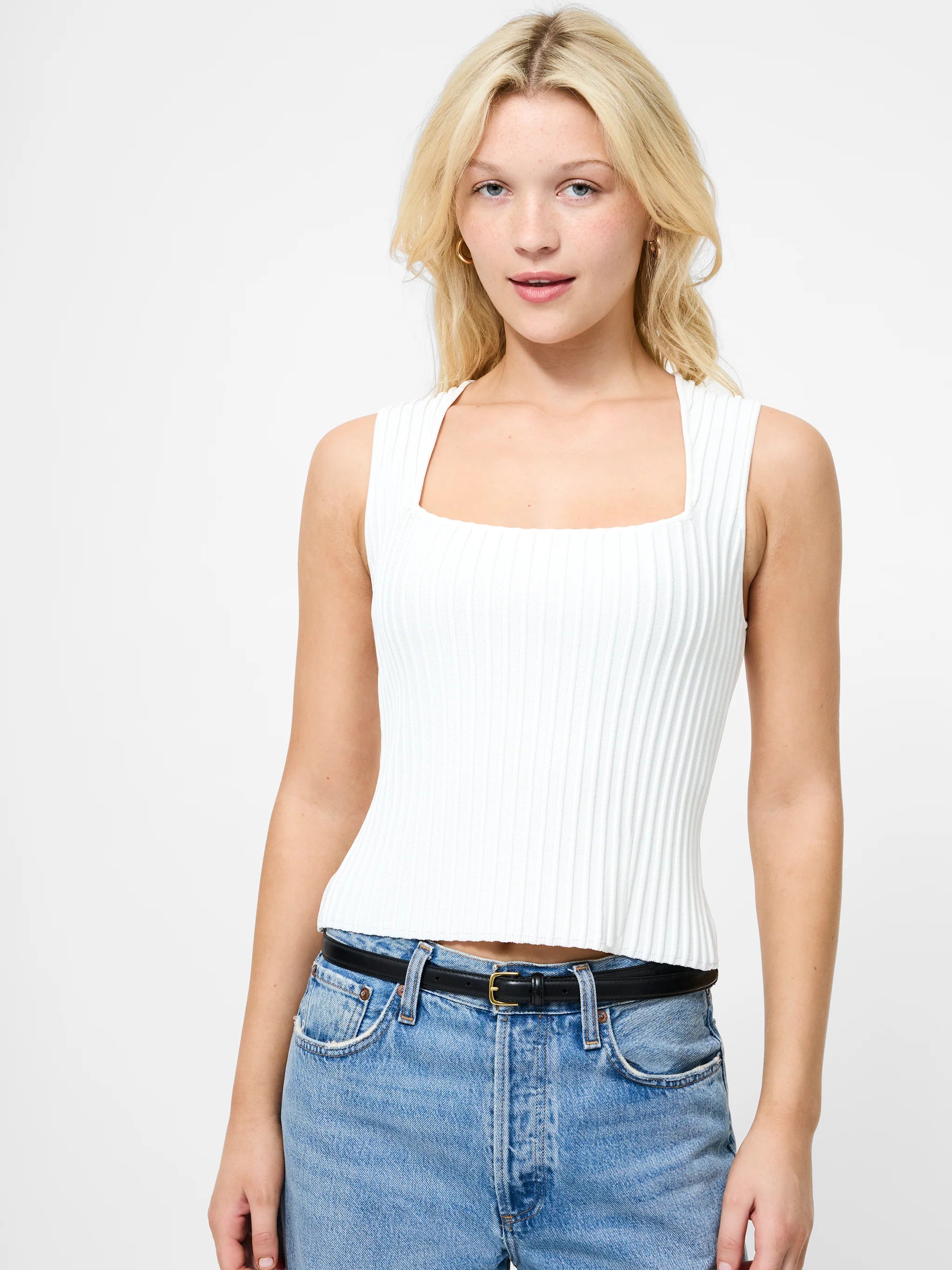 Woman wearing a white sleeveless top and blue jeans on a light gray background