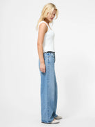 Woman wearing a white tank top and blue jeans on a white background
