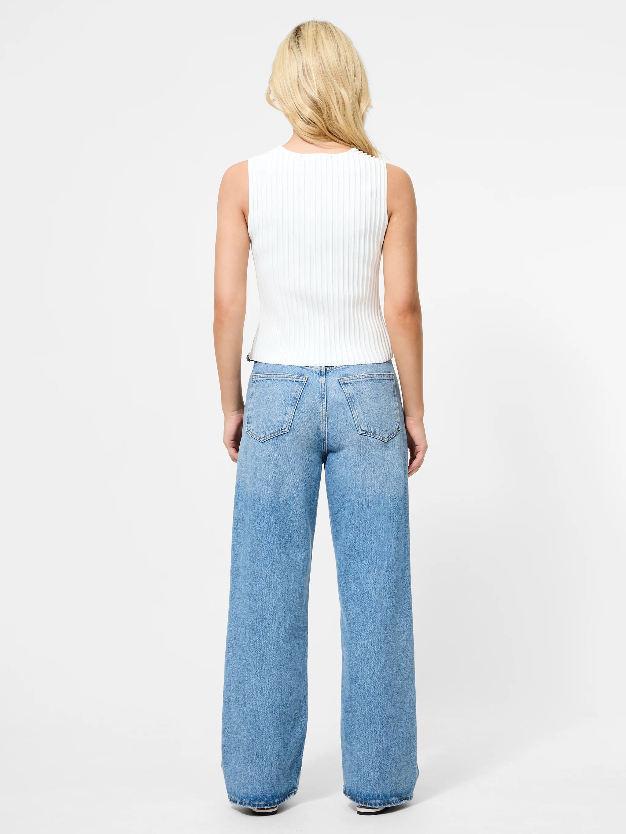 Person wearing light blue jeans and a white sleeveless top on a white background