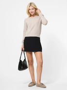 Woman wearing a beige sweater and black skirt holding a black handbag on a white background