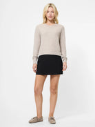 Woman wearing a beige sweater and black skirt on a white background