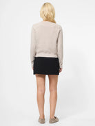 Person wearing a beige sweater and black skirt on a white background