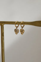 Gold heart-shaped earrings on a gold stand with a neutral background