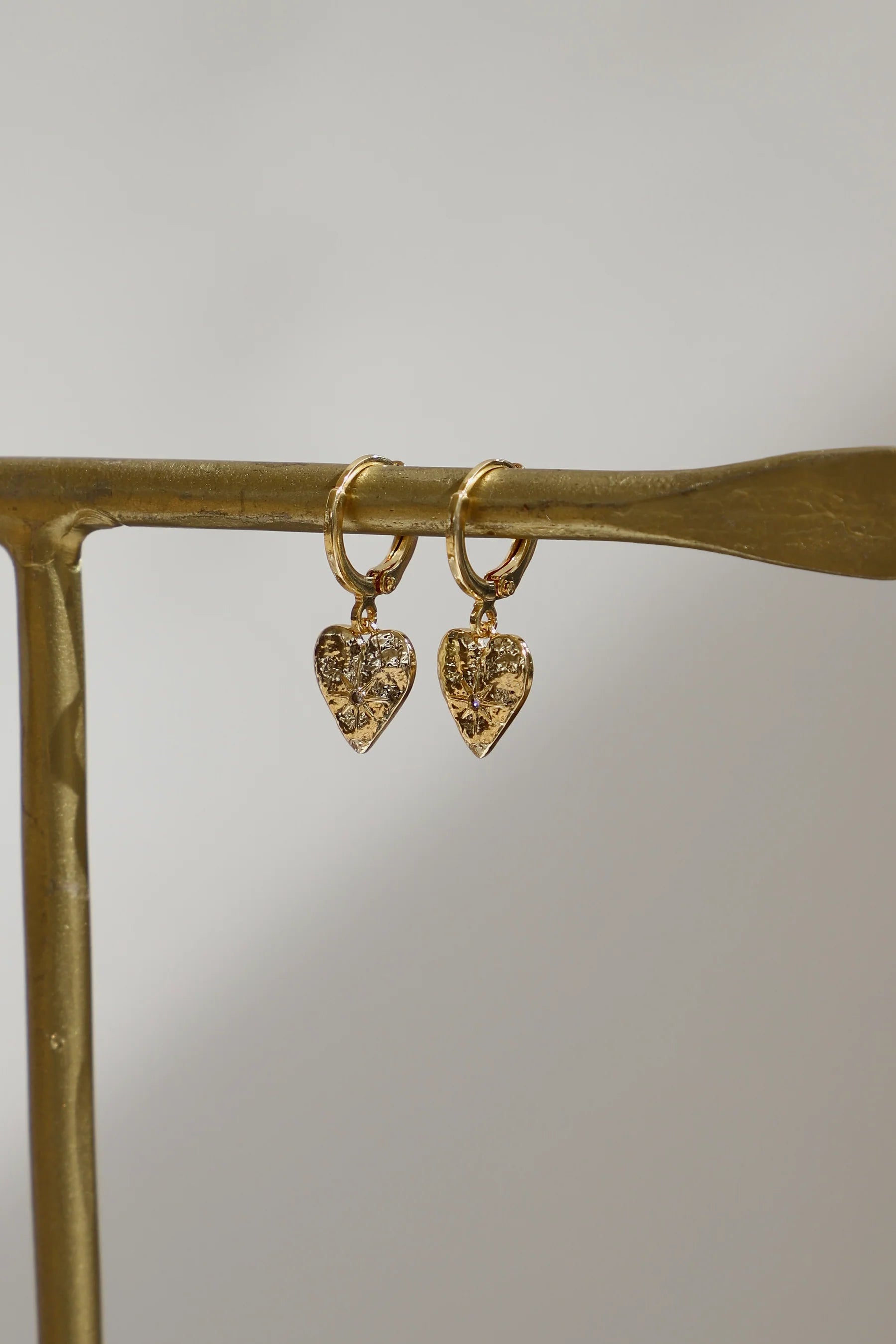 Gold heart-shaped earrings on a gold stand with a neutral background