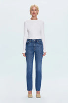 Woman wearing a white long-sleeve top and blue jeans on a light blue background