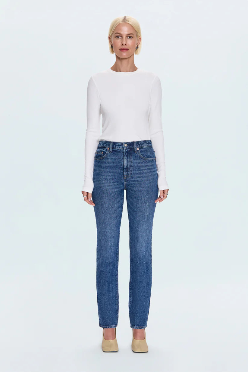 Woman wearing a white long-sleeve top and blue jeans on a light blue background