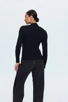 Person wearing a black long-sleeve top and black pants on a light gray background