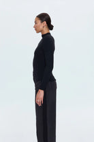 Person wearing a black turtleneck and dark pants on a white background