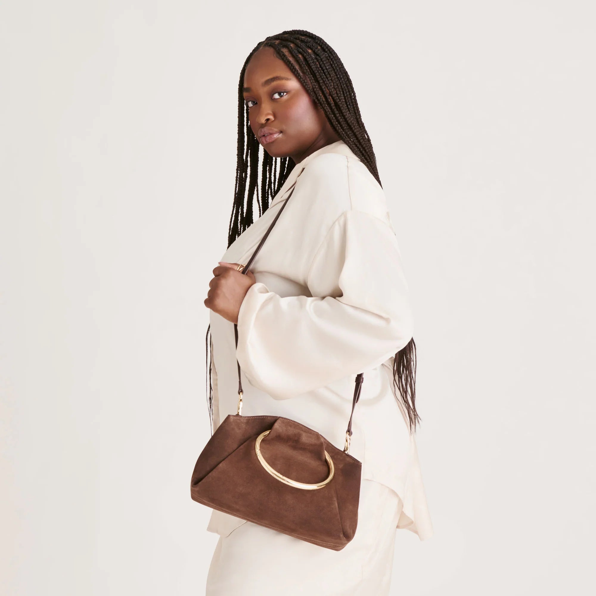 Woman holding a brown handbag against a plain background