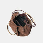 Brown suede handbag with gold circular handles on a light gray background