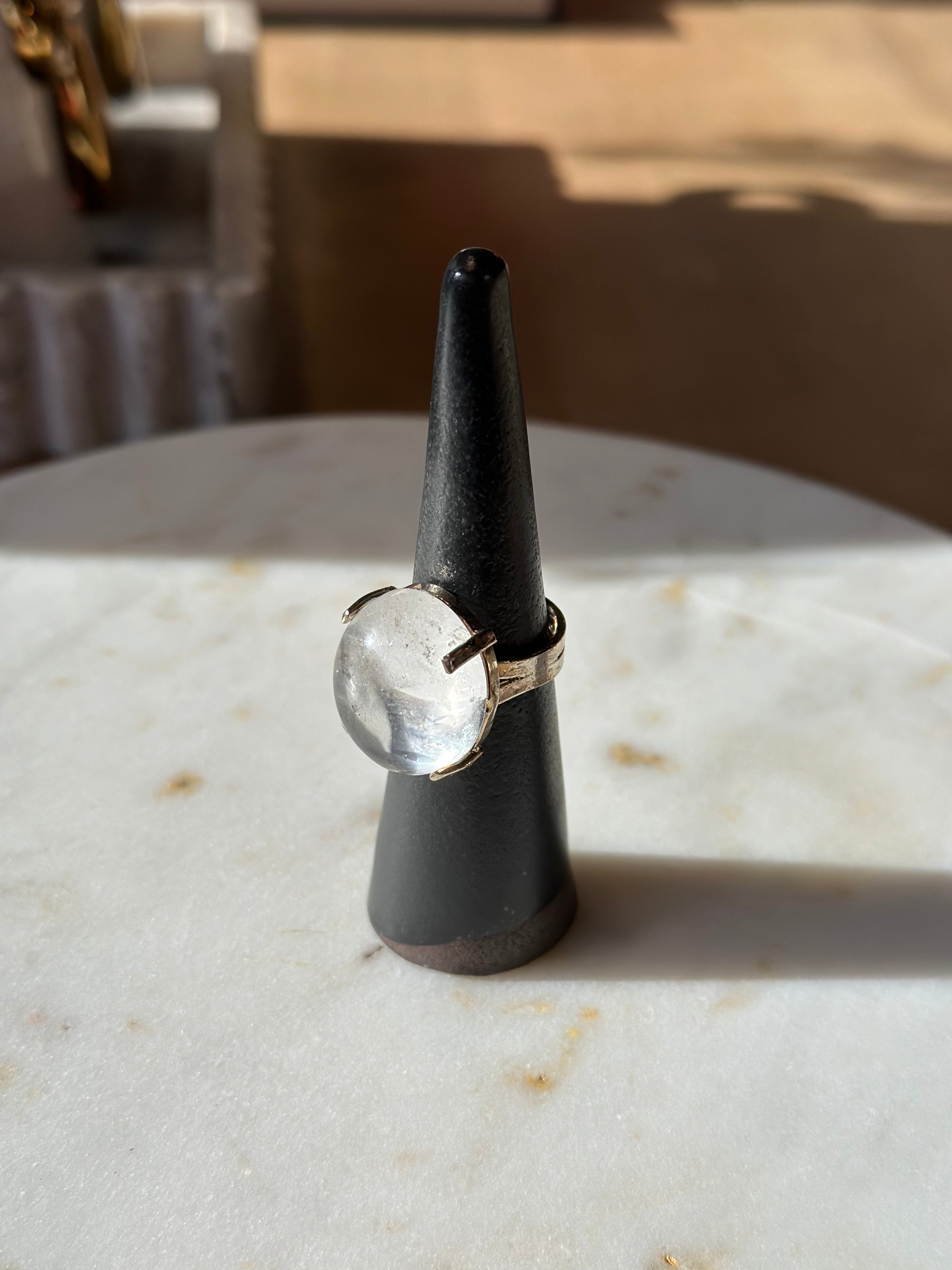 Ring with a white stone on a black stand on a marble surface