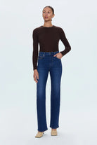 Woman wearing a brown long-sleeve top and blue jeans on a white background
