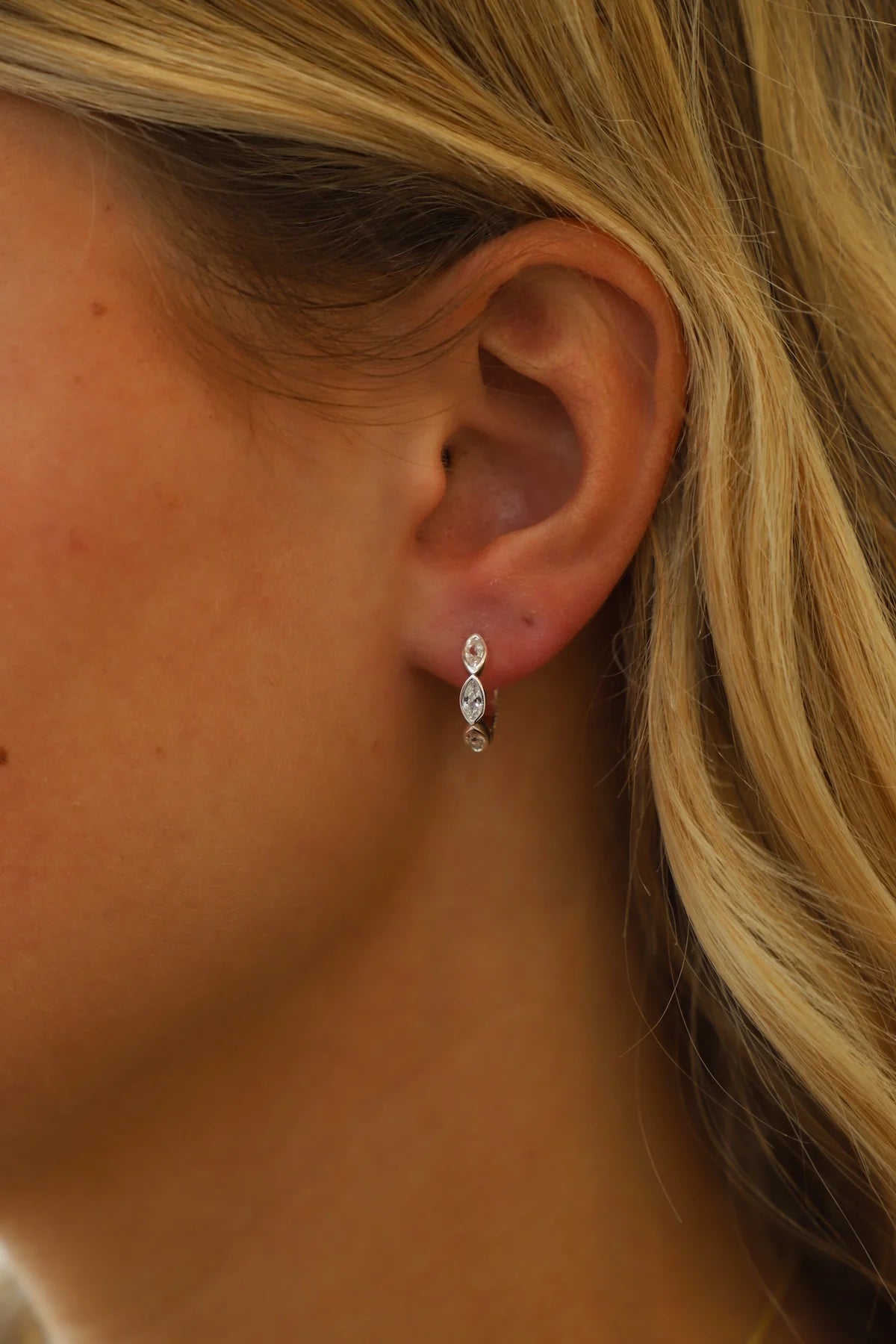 Close-up of an ear wearing a diamond earring with blonde hair.