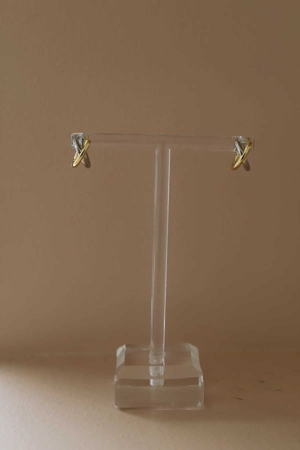 Gold earrings on a clear stand against a beige background