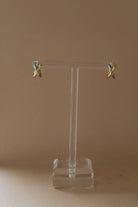 Gold earrings on a clear stand against a beige background