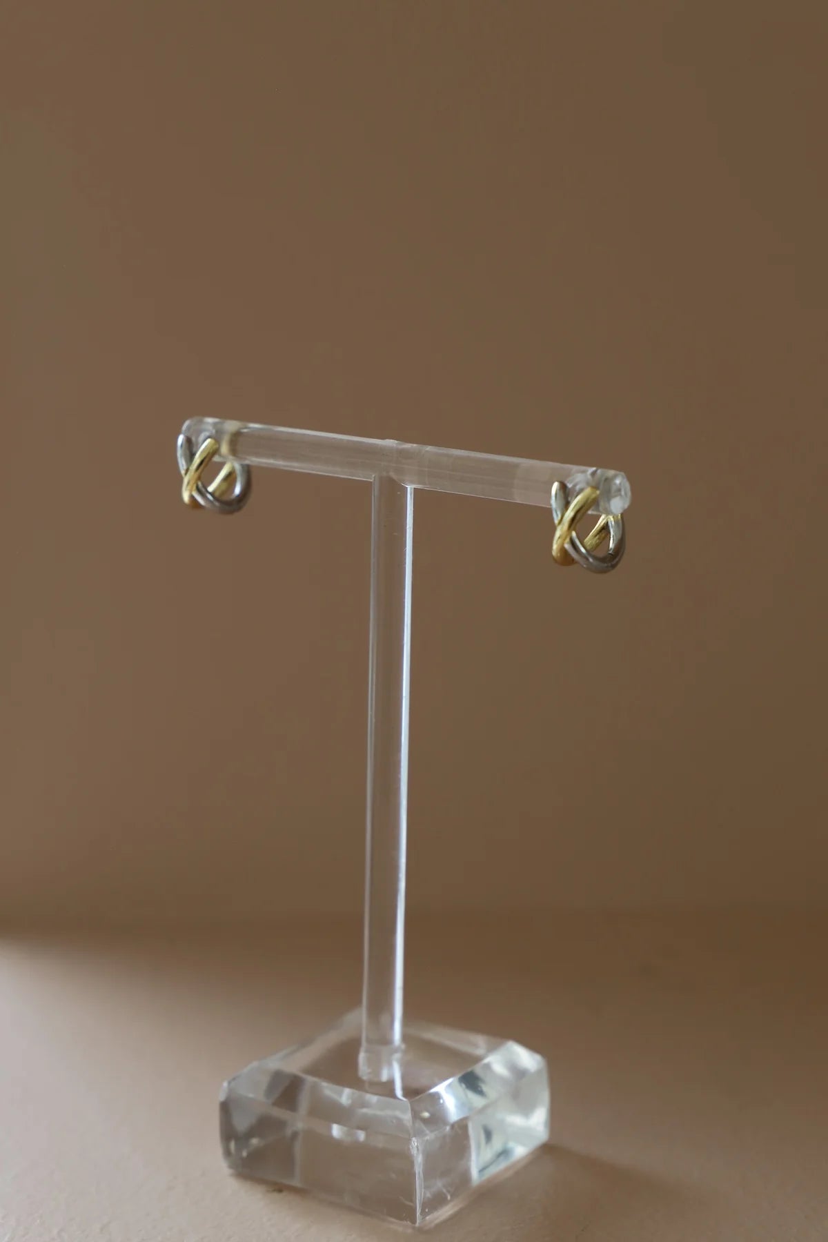 Clear earring stand with gold earrings on a brown background