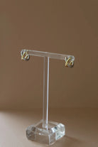 Clear earring stand with gold earrings on a brown background