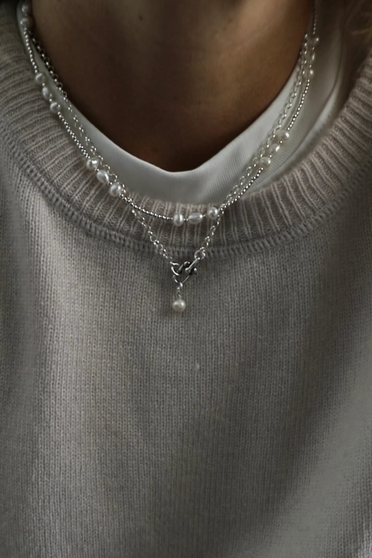 Close-up of a person wearing a gray sweater with layered pearl necklaces.
