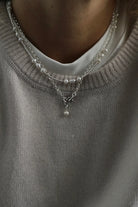 Close-up of a person wearing a gray sweater with layered pearl necklaces.