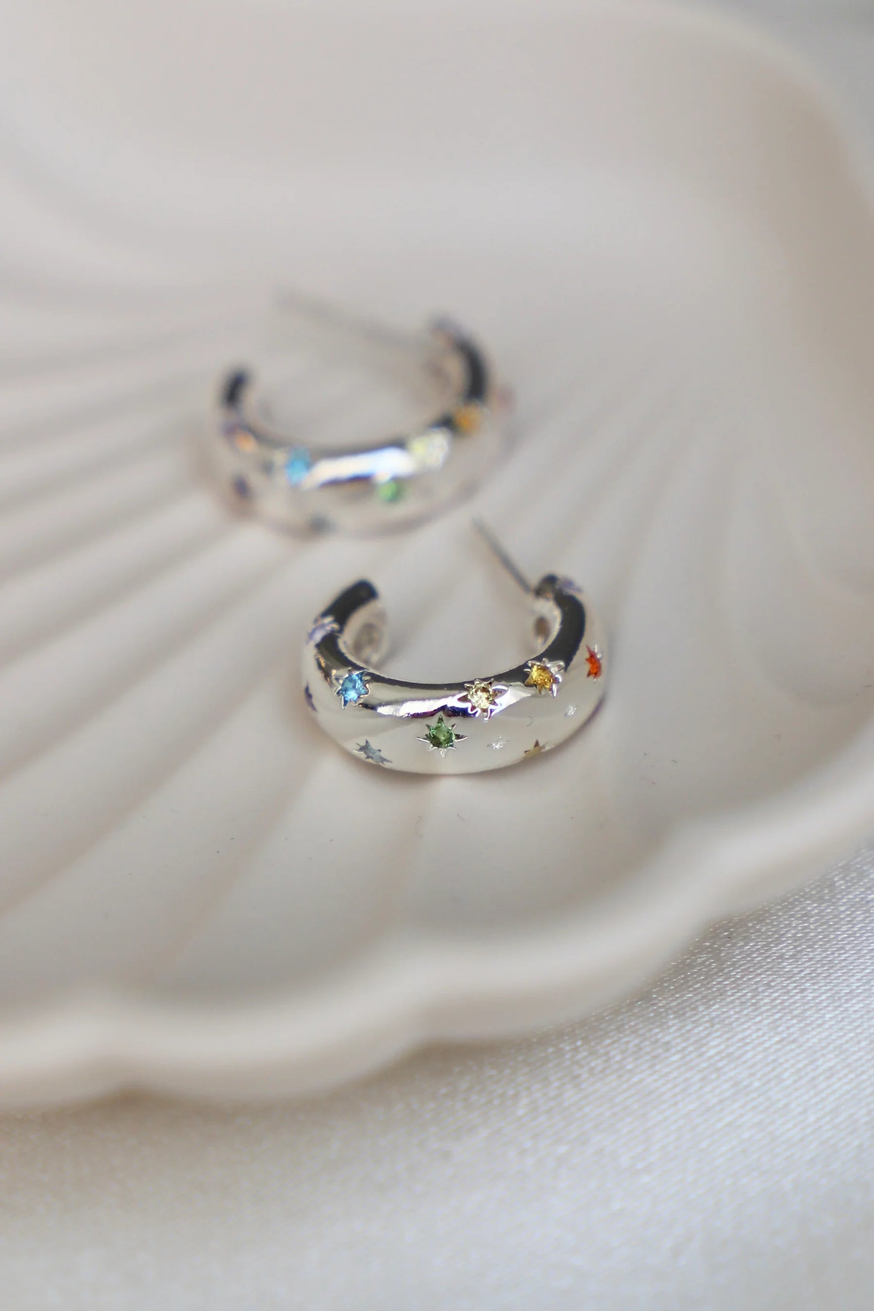 Silver hoop earrings with colorful gemstones on a white shell