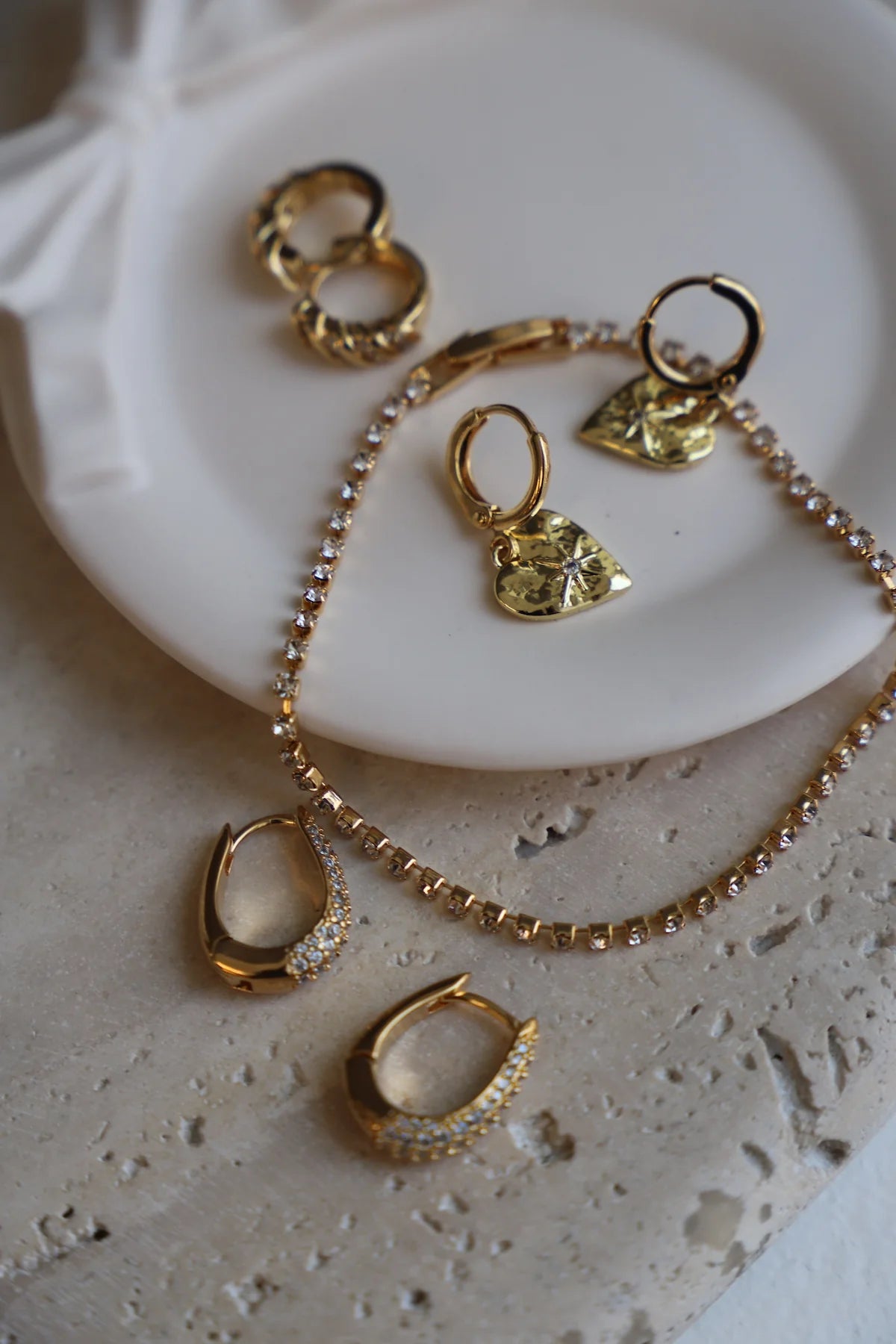 Gold jewelry set including earrings and a necklace on a white plate.