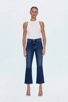 Woman wearing a white sleeveless top and blue jeans on a light gray background