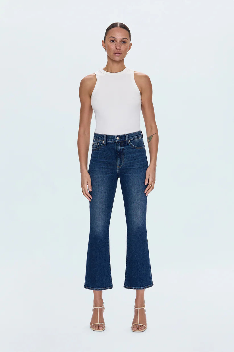 Woman wearing a white sleeveless top and blue jeans on a light gray background