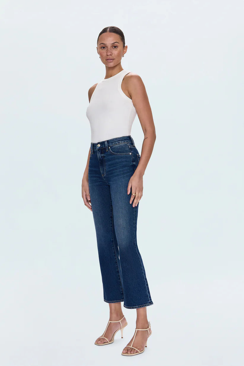 Woman wearing a white sleeveless top and blue jeans on a light gray background