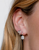 Close-up of an ear wearing a silver hoop earring with a clear gemstone.