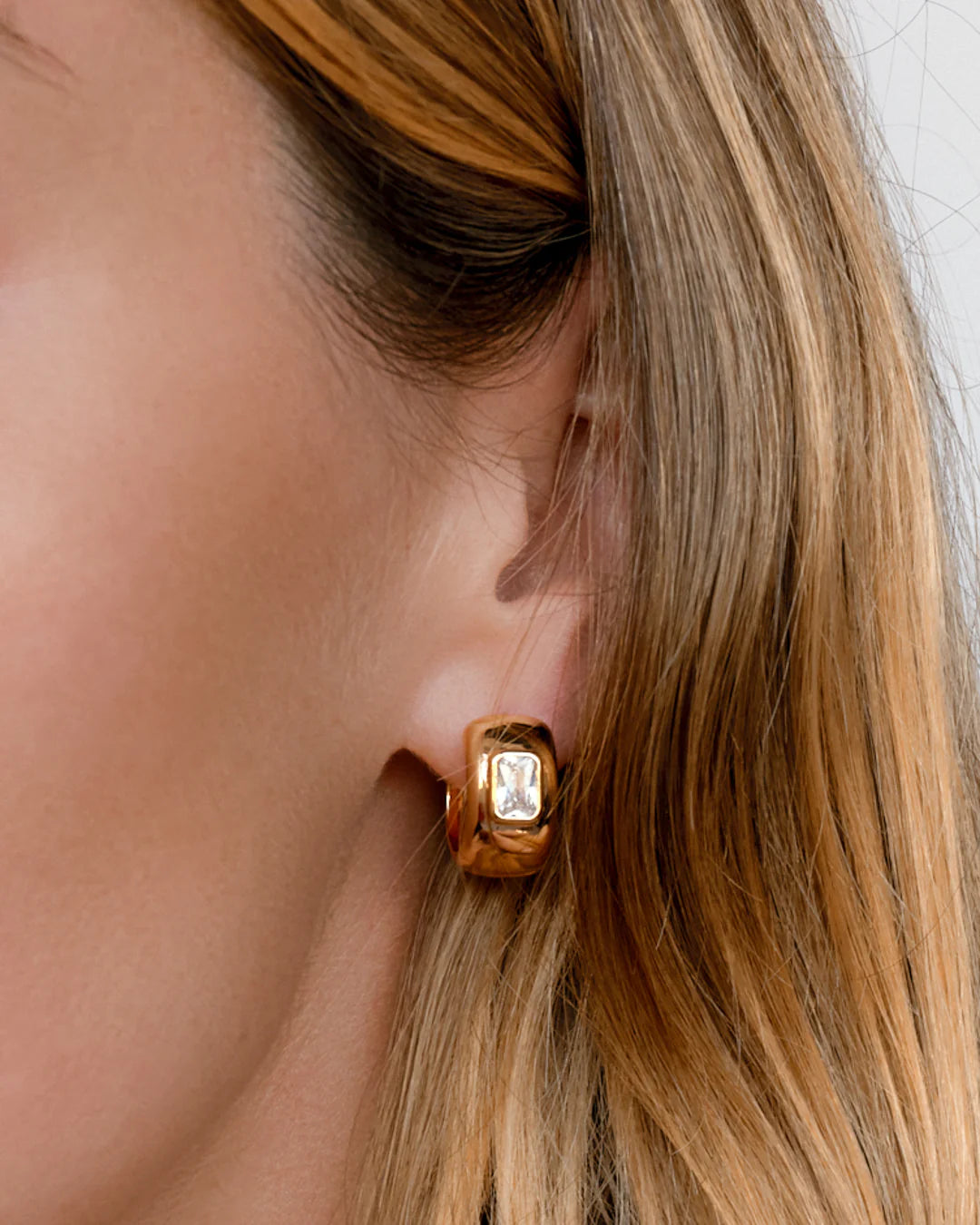 Gold earring worn by a person with blonde hair.