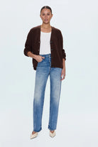 Woman wearing a brown cardigan, white top, and blue jeans on a light gray background