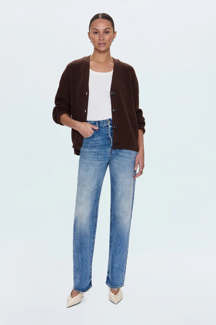 Woman wearing a brown cardigan, white top, and blue jeans on a light gray background
