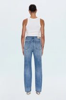 Person wearing blue jeans and a white tank top on a light gray background