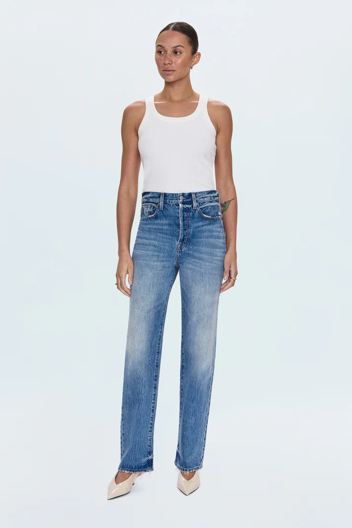 Woman wearing a white tank top and blue jeans on a light gray background