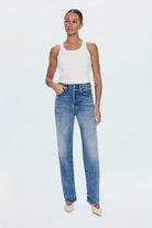 Woman wearing a white tank top and blue jeans on a light blue background