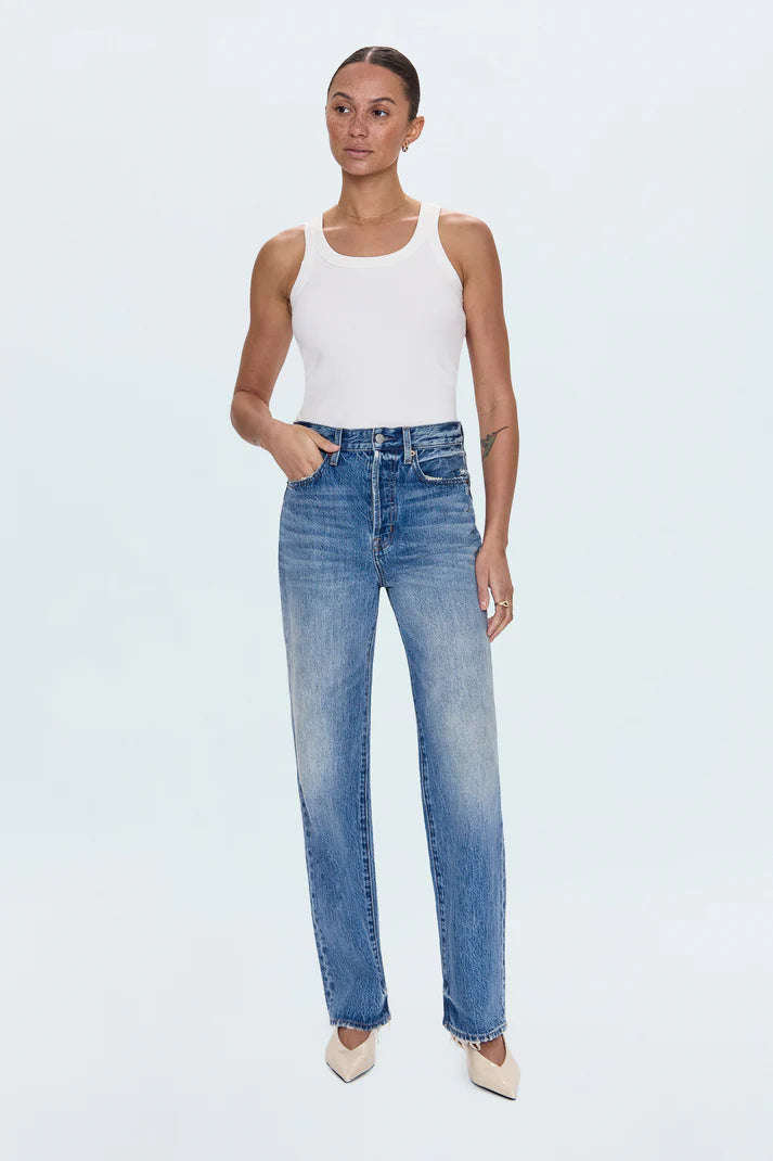 Woman wearing a white tank top and blue jeans on a light blue background