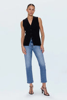 Woman wearing a black sleeveless blazer and blue jeans on a white background