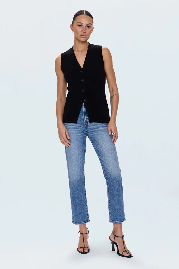 Woman wearing a black sleeveless blazer and blue jeans on a white background