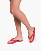 Red flip-flops worn on feet against a white background
