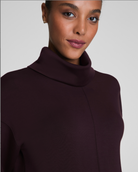 Woman wearing a dark brown turtleneck sweater against a plain background
