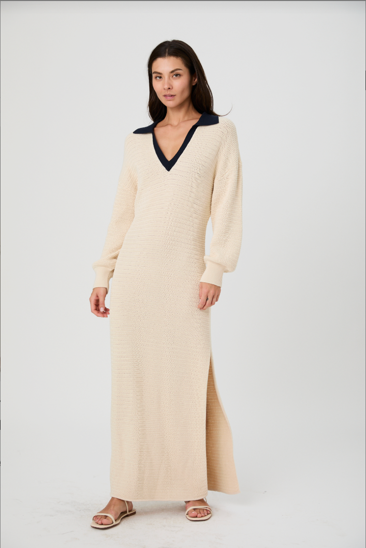 Woman wearing a long cream dress with a black collar on a white background