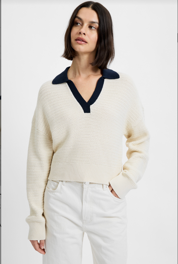 Woman wearing a cream sweater with a navy collar against a white background