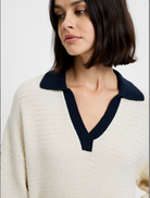 Woman wearing a white sweater with a navy collar on a plain background