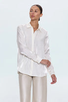 Woman wearing a white blouse and beige pants against a light blue background