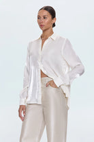Woman wearing a white blouse and beige pants against a light blue background