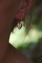 Close-up of a person wearing gold heart-shaped earrings with a blurred green background